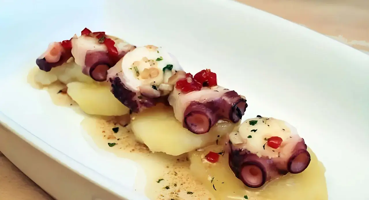Delicioso carpaccio de pulpo con patatas cocidas, adornado con pimientos rojos picados y hierbas frescas.