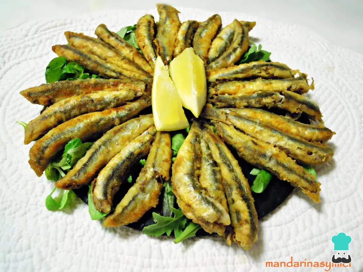 Deliciosos boquerones en adobo, crujientes y dorados, servidos con gajos de limón y hojas verdes.