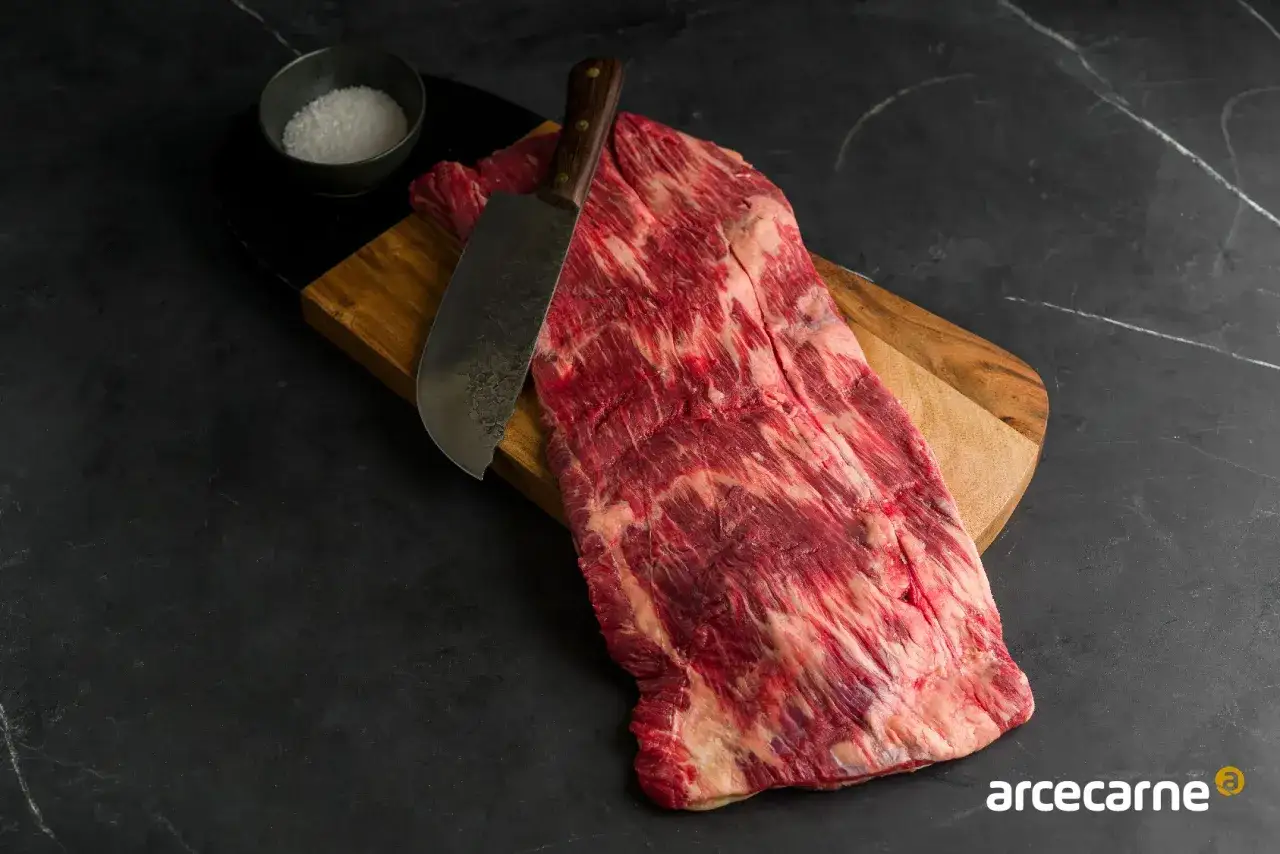 Un corte de brisket crudo, marmoleado y listo para cocinar, con un cuchillo y sal en un tazón.