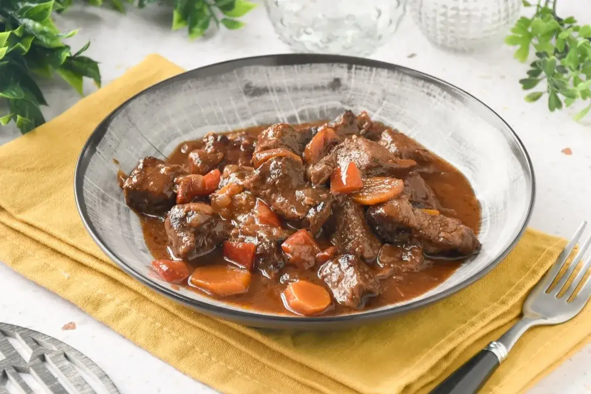 Un plato humeante de carne al toro, tierna y jugosa, con trozos de zanahoria y pimiento en una rica salsa.