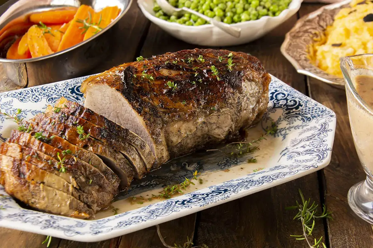 Un jugoso churrasco al horno, recién cortado y adornado con hierbas frescas, listo para acompañar con zanahorias y puré.
