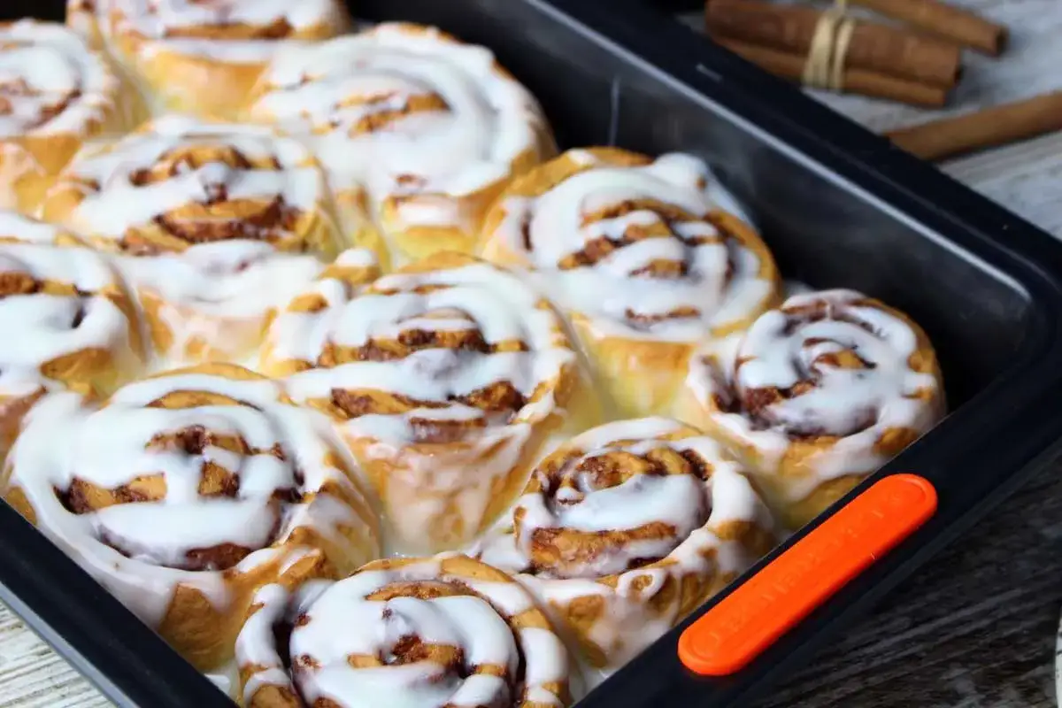 Rollo de canela reci&eacute;n horneados, cubiertos con glaseado blanco cremoso, listos para disfrutar.