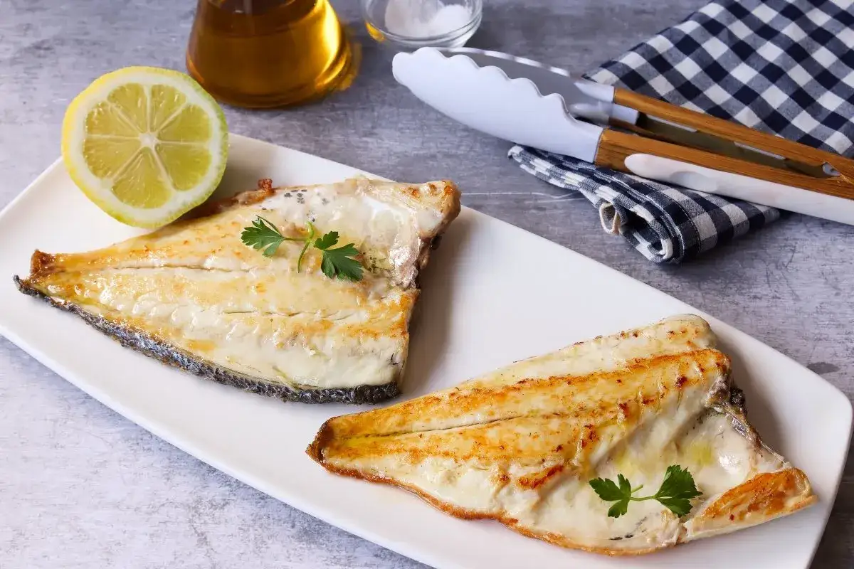 Dos filetes de dorada a la plancha, jugosos y dorados, servidos con lim&oacute;n y perejil.
