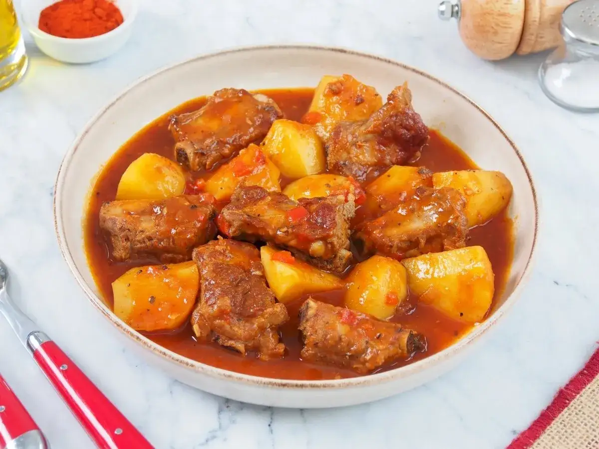 Un plato humeante de patatas con costillas en una rica salsa roja. Las patatas están cortadas en trozos grandes y las costillas tiernas se ven deliciosas.