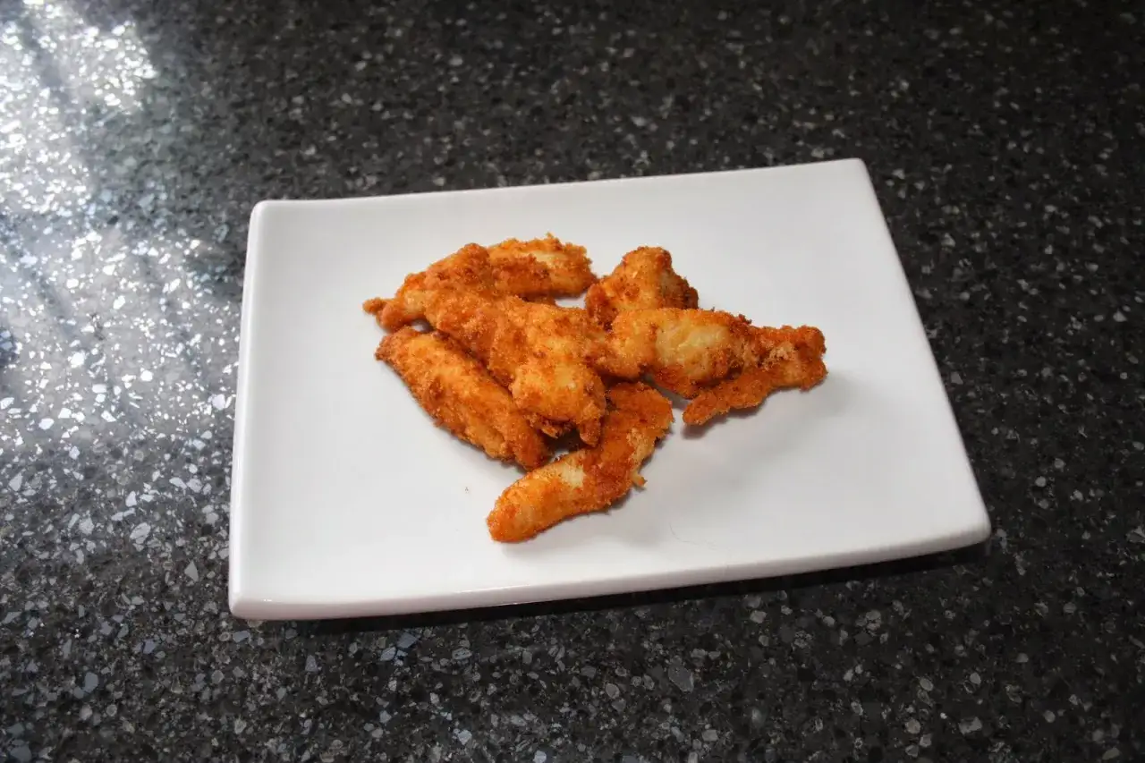 Un plato blanco con lagrimitas de pollo crujientes y doradas.