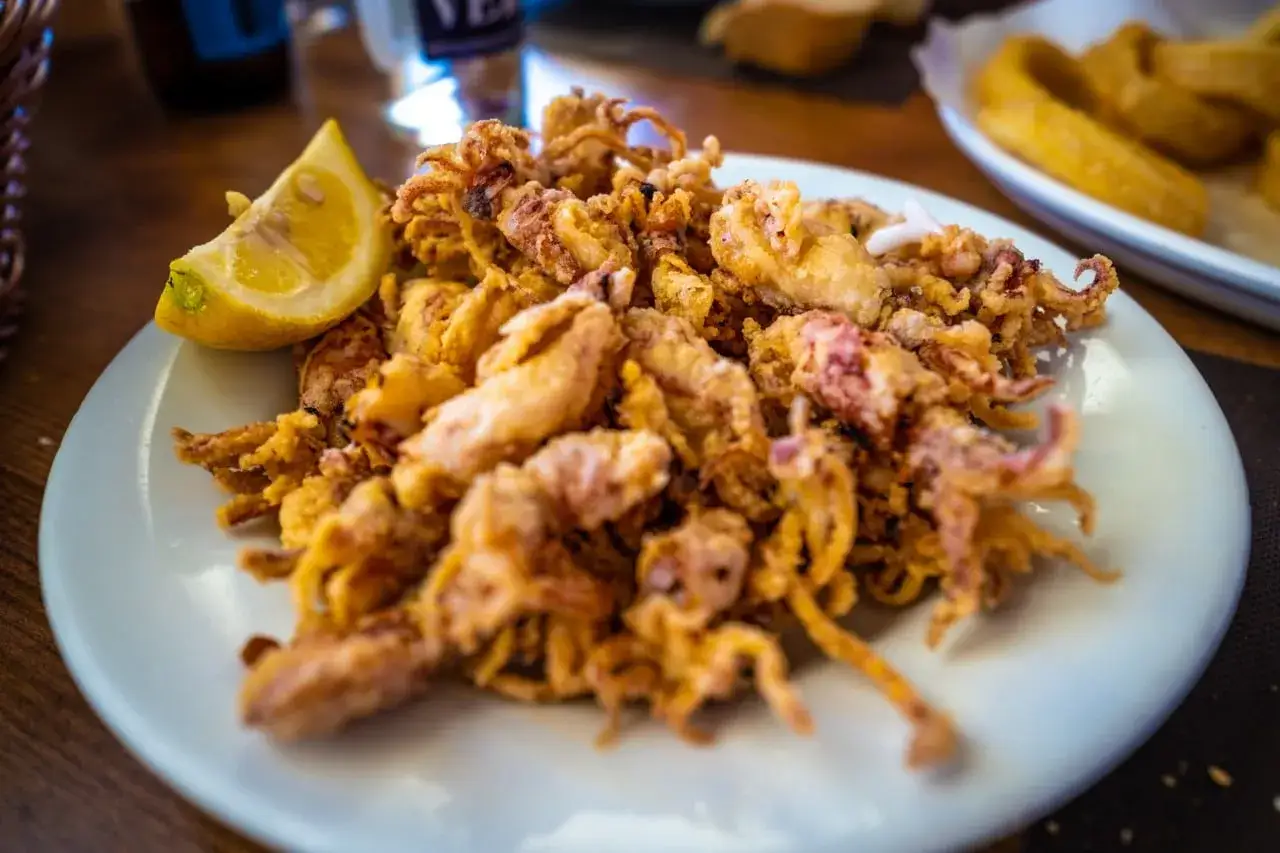 Un plato de puntillas de calamar crujientes y doradas, servido con una rodaja de limón fresco.