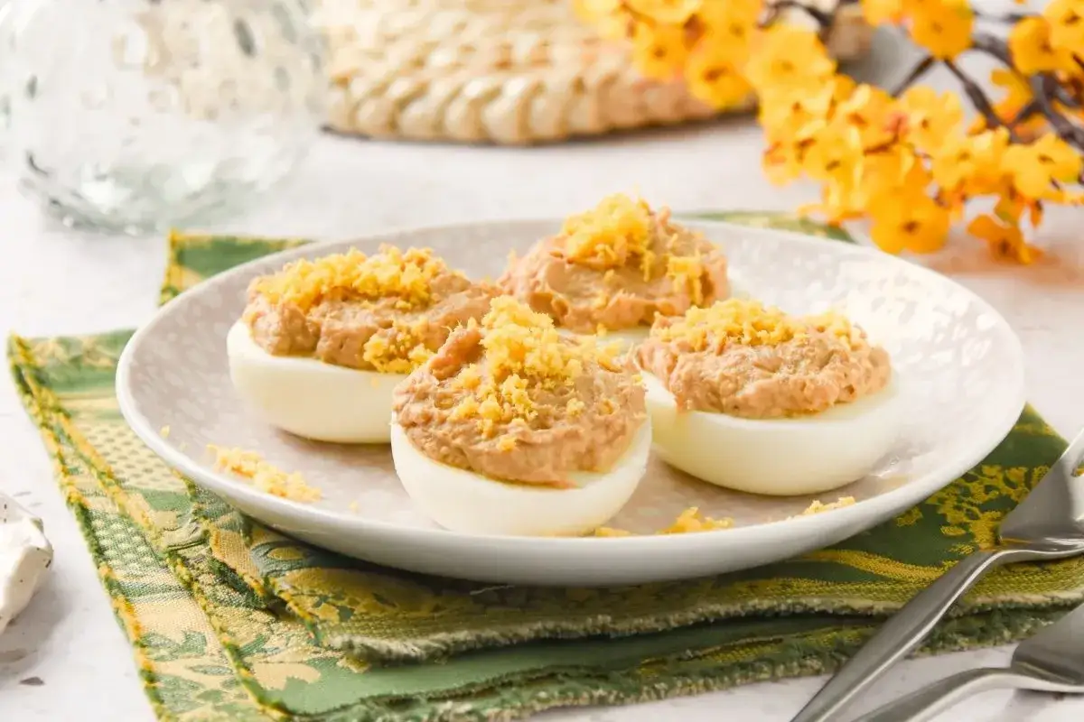 Huevos rellenos de atún cremosos, espolvoreados con ralladura amarilla, en un plato blanco.