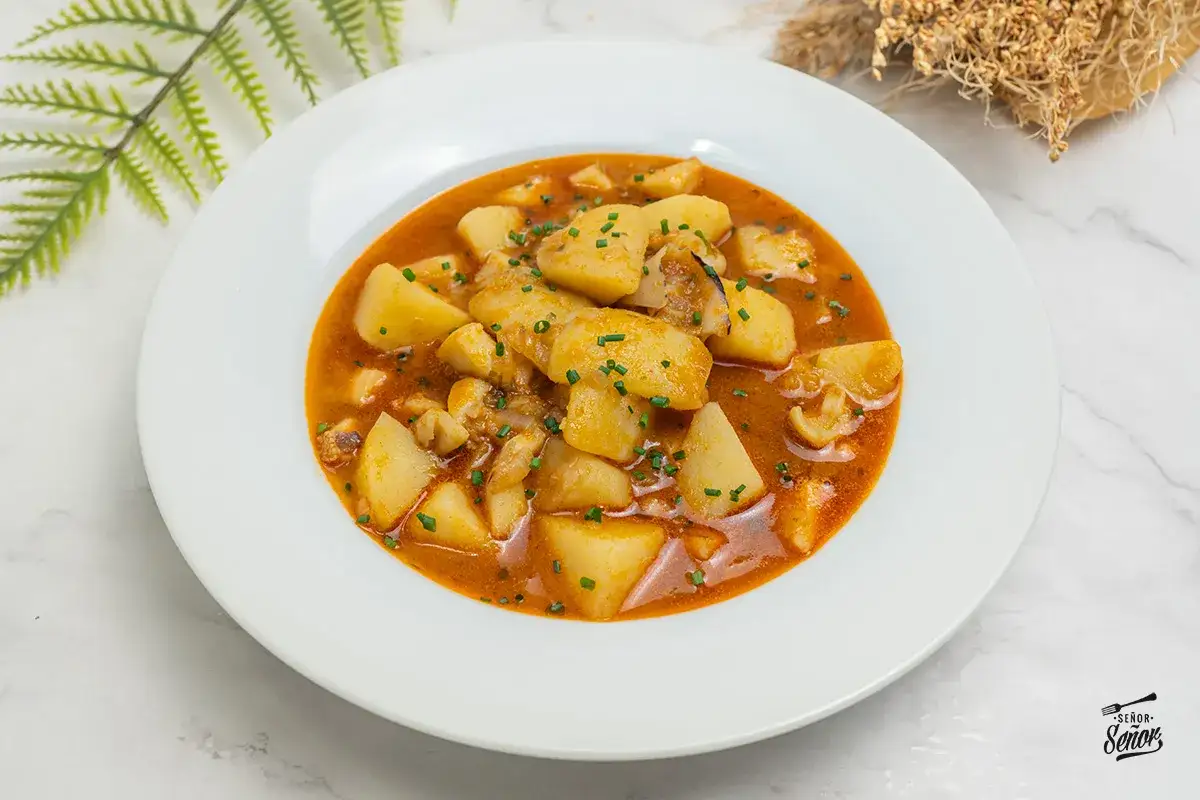 Plato de patatas con sepia, un guiso casero que recuerda a las patatas con sepia de la abuela, con trozos de patata y sepia en una salsa rojiza.