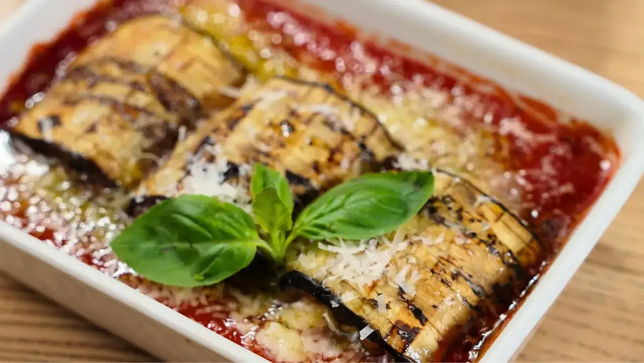 Delicioso pastel de berenjenas gratinado con queso y salsa de tomate, adornado con hojas de albahaca fresca.