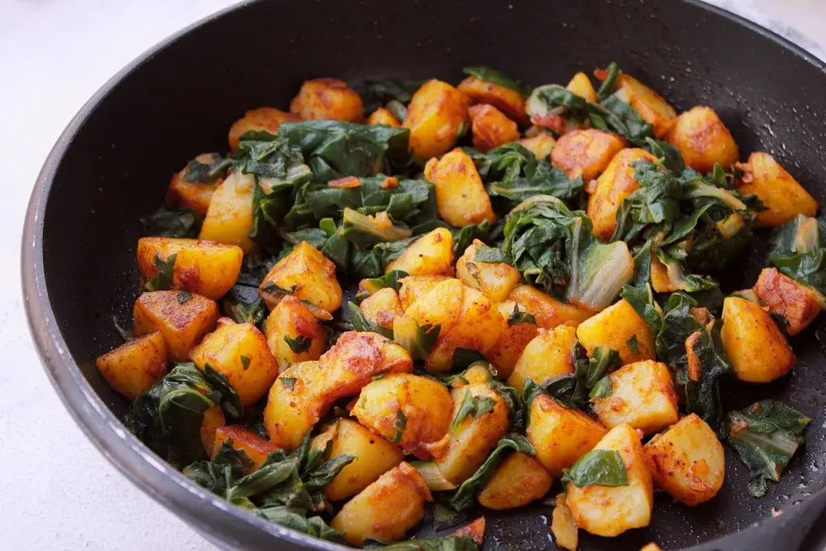 Sabrosas acelgas con patatas doradas en una sart&eacute;n, un plato casero lleno de sabor y color.