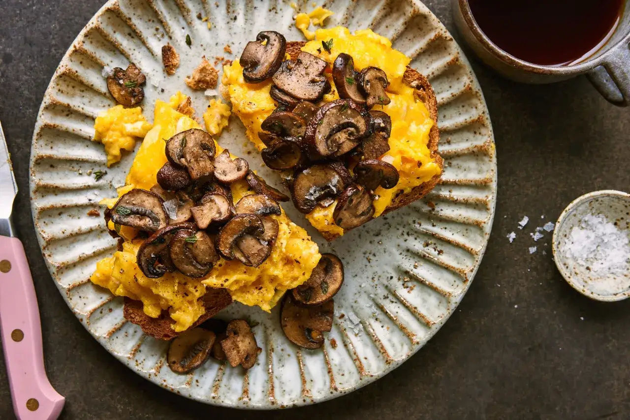 Tostadas con revuelto de champiñones y hierbas, servidas en plato rústico. Un desayuno delicioso y nutritivo.