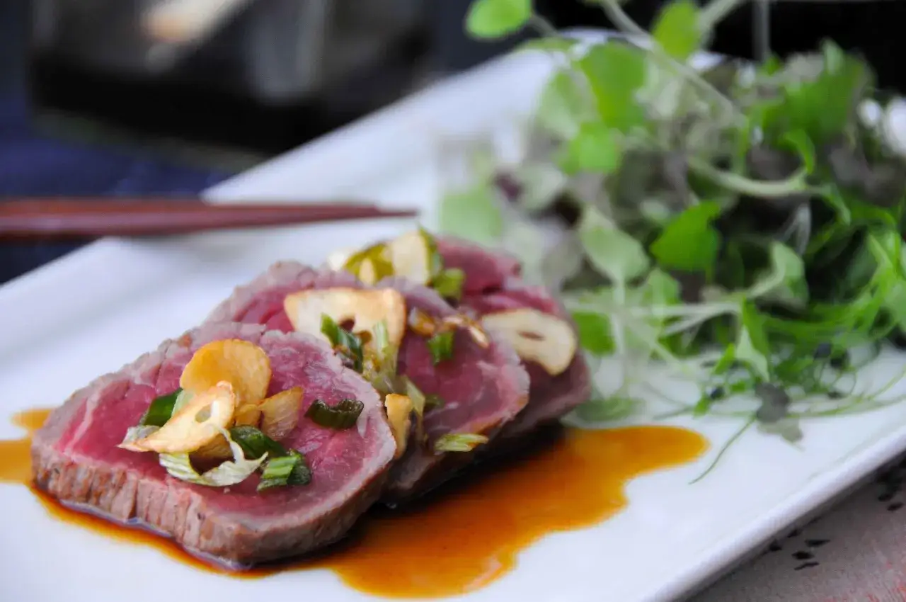 Tataki de ternera con crujientes de ajo y cebolleta, acompañado de una ensalada fresca.