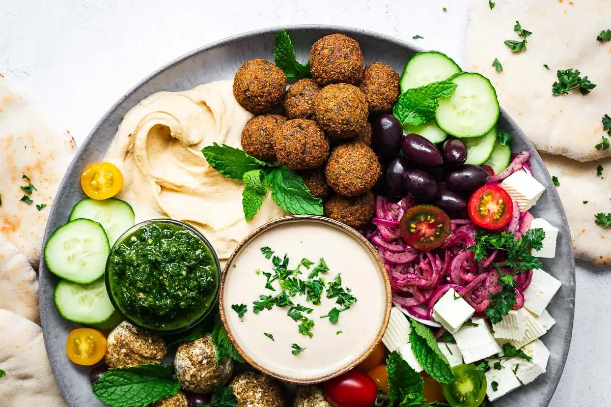 Tabla de falafel que es: bolitas doradas, hummus cremoso, pepino, aceitunas, queso feta y salsas.