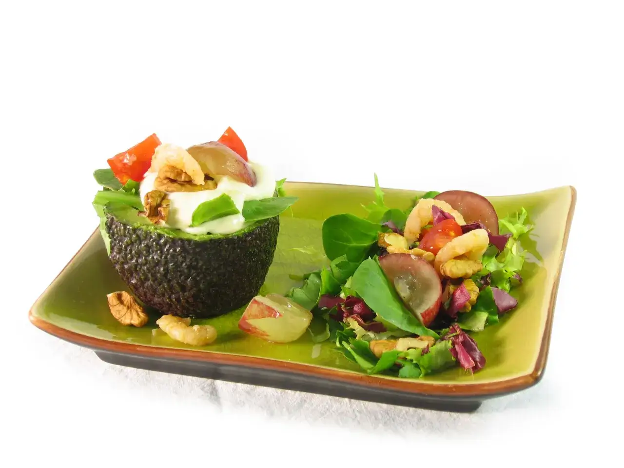 Aguacate relleno con ensalada, camarones, uvas y nueces en plato verde.