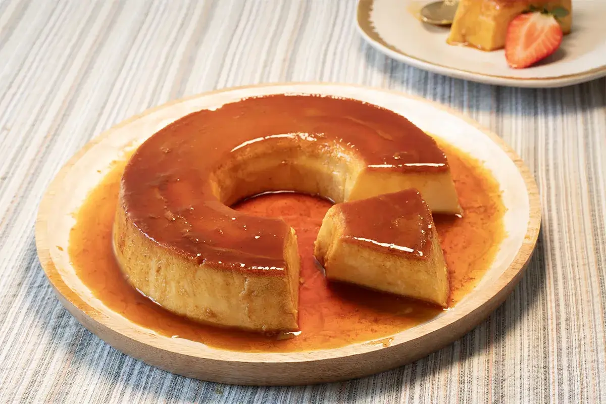 Un delicioso flan de leche condensada con caramelo líquido, servido en un plato de madera.