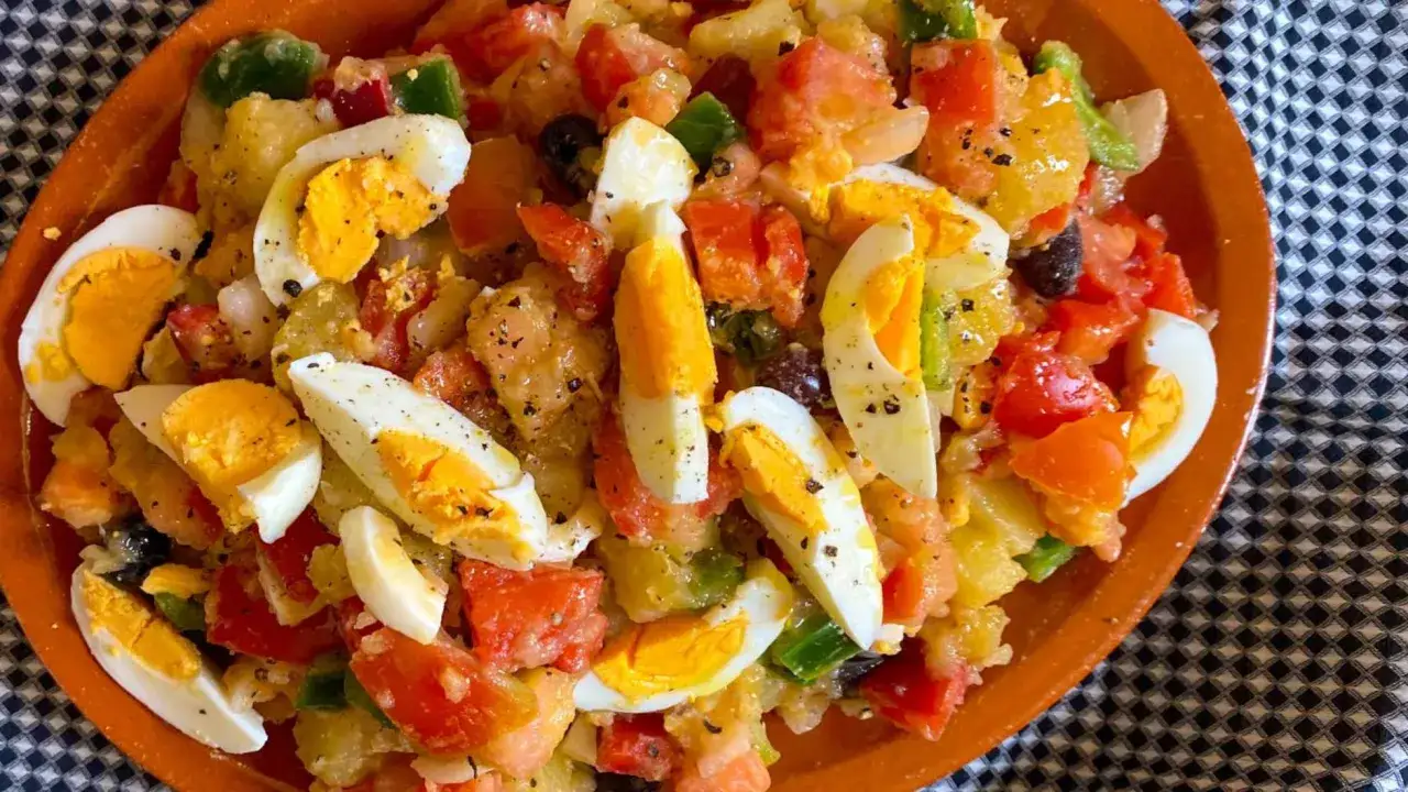 Ensalada campera con patatas, tomates, pimientos, aceitunas y huevos duros, servida en una cazuela de barro.