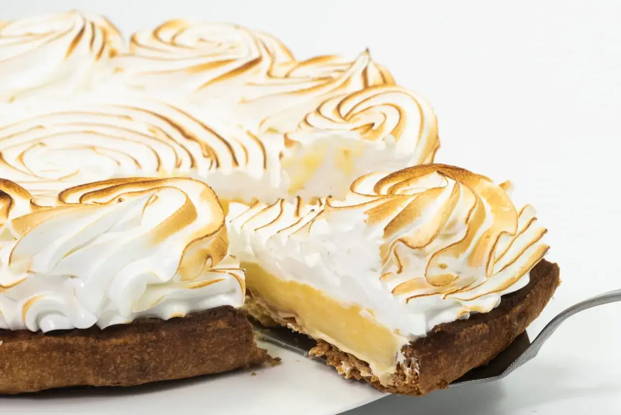 Tarta de lim&oacute;n con merengue dorado, con una porci&oacute;n servida en una pala.
