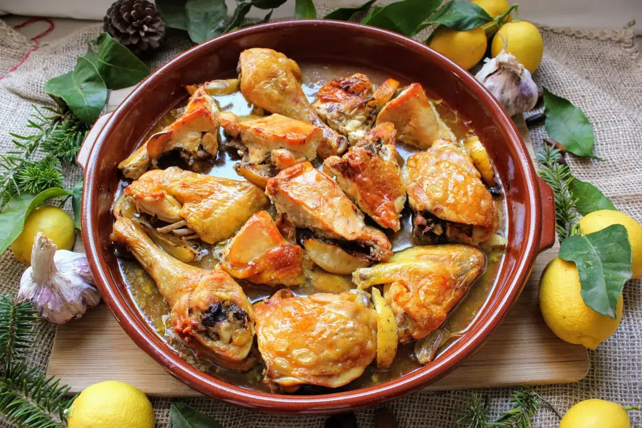 Delicioso pollo al ajillo en cazuela de barro, rodeado de limones, ajos y romero.
