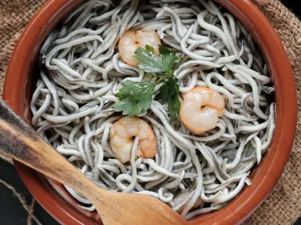 Deliciosas recetas con gulas y gambas, servidas en cazuela de barro con perejil y cuchara de madera.