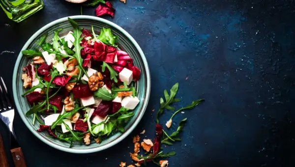 Ensalada de remolacha vibrante con queso feta, nueces y rúcula en un plato azul.