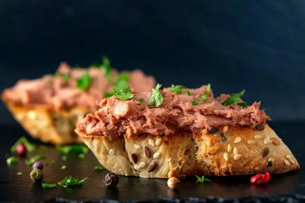 Rebanadas de pan rústico con un generoso untado de paté de hígado de pollo, decorado con perejil fresco y granos de pimienta.