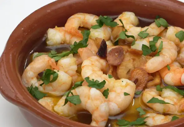 Gambas al pil pil burbujeantes en cazuela de barro, con ajo dorado y perejil fresco.