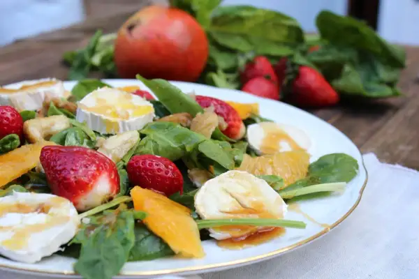Deliciosa ensalada de espinacas con fresas, naranja, queso de cabra y nueces, bañada en aderezo dulce.