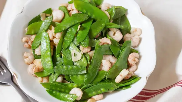 Plato de tirabeques salteados con gambas y ajo. Los tirabeques, crujientes y verdes, se mezclan con las gambas rosadas y láminas de ajo.