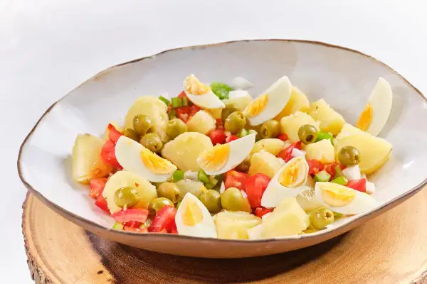 Ensalada campera con patatas, huevos cocidos, tomates y aceitunas verdes, servida en un cuenco rústico.