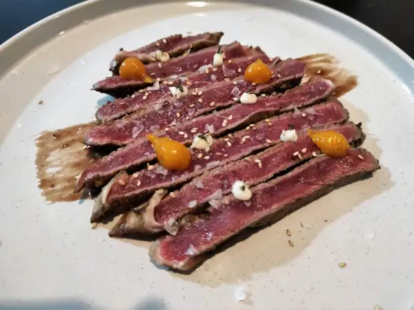 Tataki de ternera, finas lonchas de carne rosada con sésamo, sal gorda y toques de salsa y puré de mango.