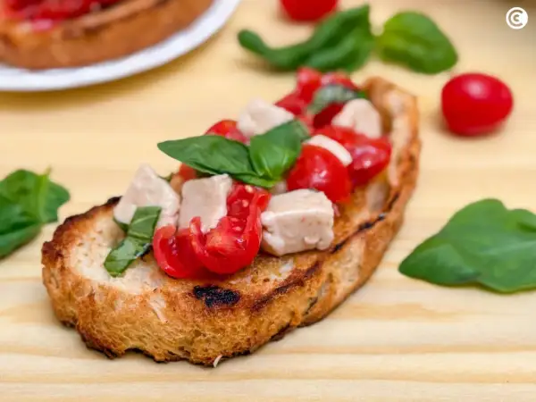 Una bruschetta que es un pan tostado cubierto con tomates frescos, cubos de mozzarella y hojas de albahaca verde.