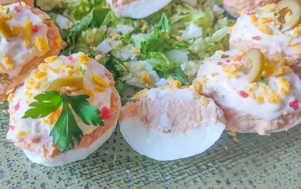 Deliciosos huevos rellenos adornados con aceitunas, perejil y trocitos de huevo duro, servidos sobre una cama de lechuga fresca.