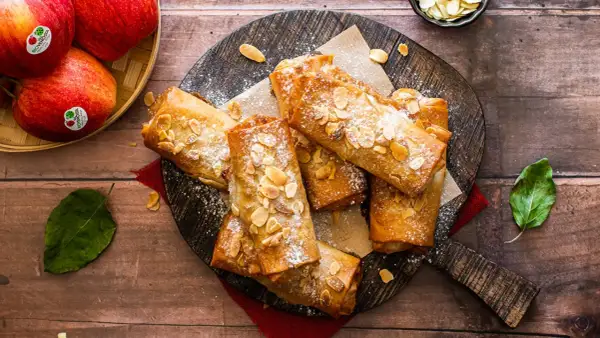 Deliciosos rollos de strudel de manzana dorados, espolvoreados con azúcar glas y almendras fileteadas, listos para disfrutar.