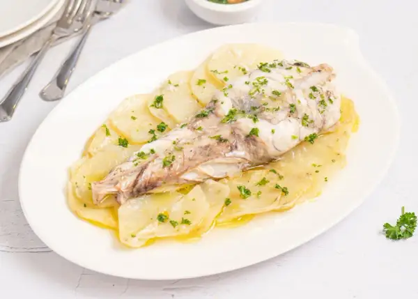 Delicioso rape al horno sobre cama de patatas laminadas, espolvoreado con perejil fresco.
