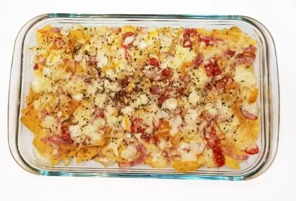 Nachos con queso horneados, cubiertos con trozos de tocino y pimientos rojos.