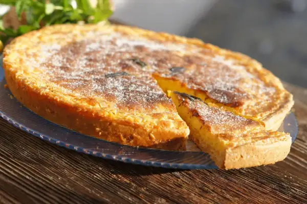 Un delicioso postre típico de Ibiza, una tarta dorada espolvoreada con azúcar glas, con una porción cortada.