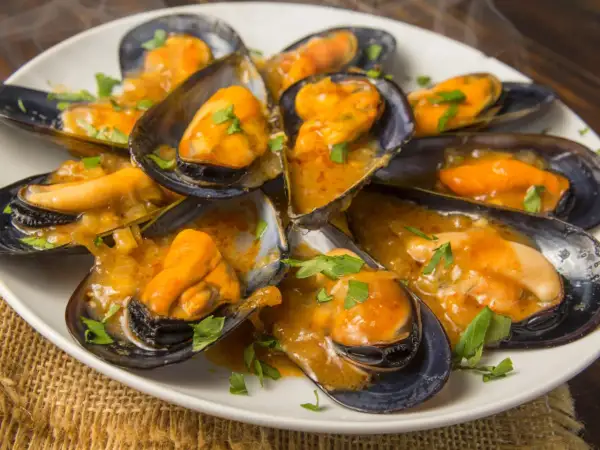 Mejillones en salsa, como los de los bares, servidos en una cazuela blanca con perejil picado.