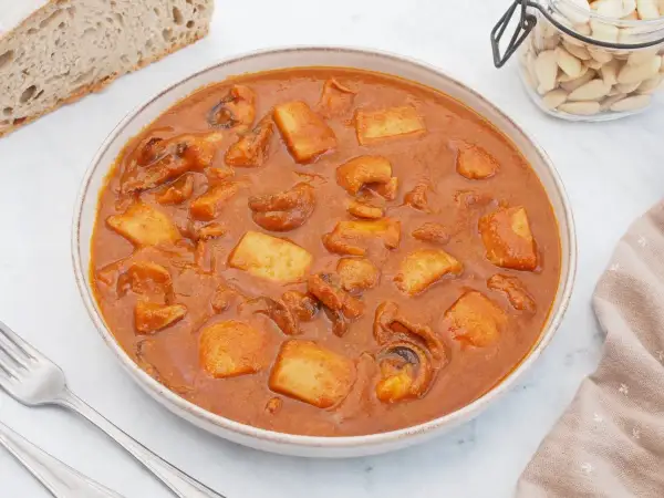Un plato humeante de jibia en salsa, con trozos de patata y pan rústico al lado.