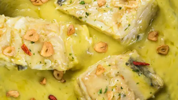 Merluza al pil pil, jugosos trozos de pescado blanco en una salsa cremosa con láminas de ajo crujiente y guindilla.