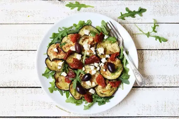 Deliciosa ensalada de berenjena asada con rúcula, tomates secos, aceitunas negras y queso feta.