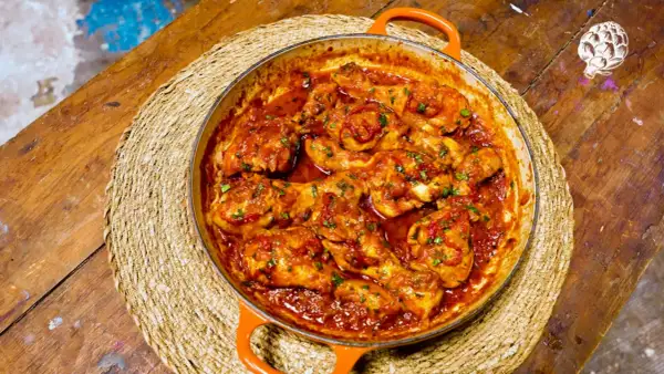 Pollo a la toledana en cazuela naranja, servido sobre una esterilla de mimbre en una mesa de madera rústica.