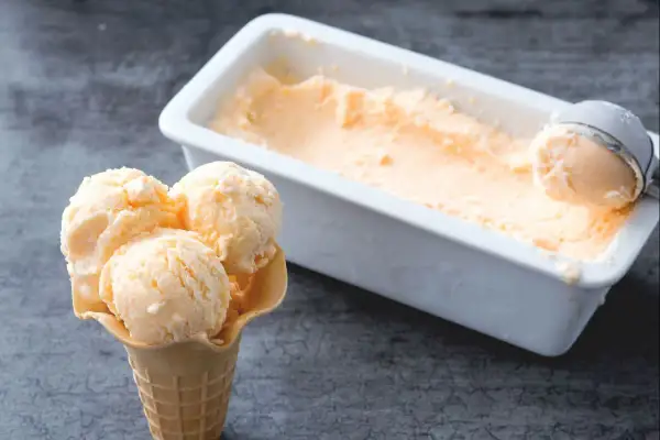 Un cono con tres bolas de helado de melón cremoso y una cubeta llena de este refrescante postre.