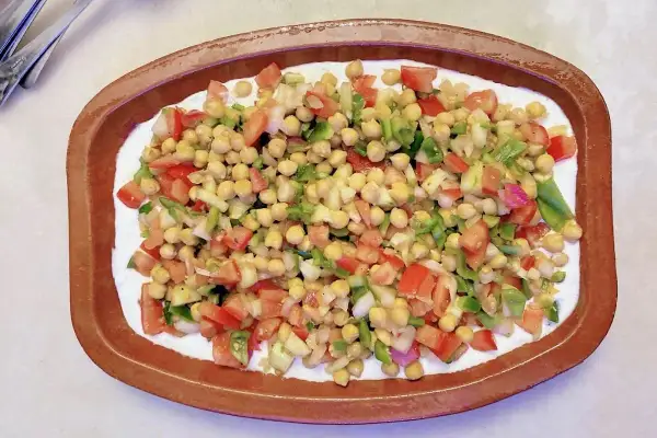 Deliciosa ensalada de garbanzos con tomate, pimiento y cebolla, servida sobre una base cremosa en un cuenco de barro.