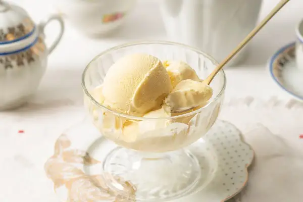 Copa de cristal con cremoso helado de mantecado, lista para disfrutar. Una cuchara dorada toma una porción.