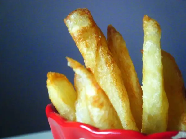 Patatas fritas doradas y crujientes en un recipiente rojo.