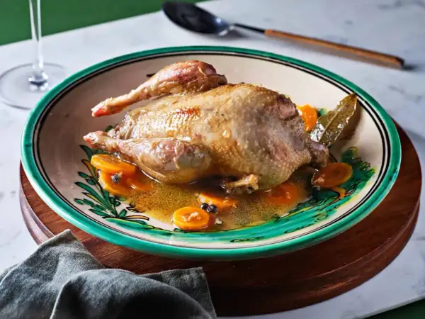 Perdiz a la toledana servida en plato decorado con rodajas de zanahoria y especias.