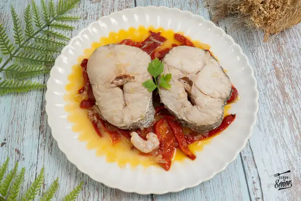 Dos rodajas de merluza a la riojana, servidas sobre pimientos rojos y una gamba, decoradas con perejil.