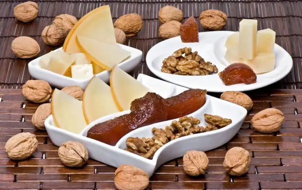 Queso y nueces acompañan trozos de dulce de manzana en una tabla de madera.