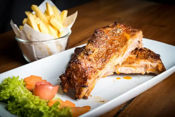 Costillas de cerdo al horno jugosas y doradas, acompañadas de papas fritas crujientes y una guarnición fresca.