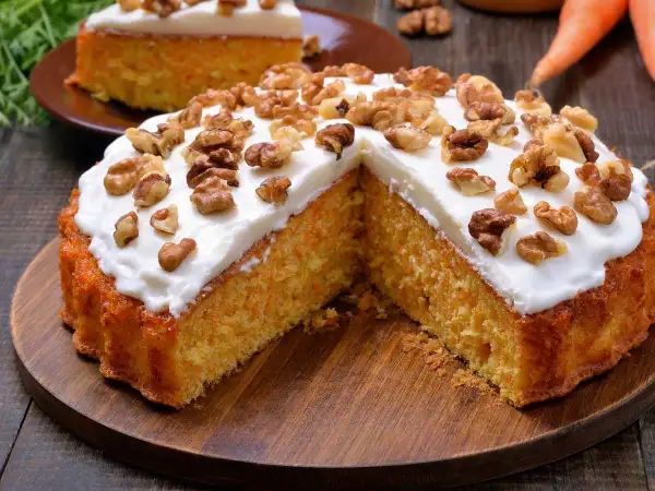 Un delicioso bizcocho de zanahoria, cubierto con glaseado blanco y nueces, servido en una tabla de madera.
